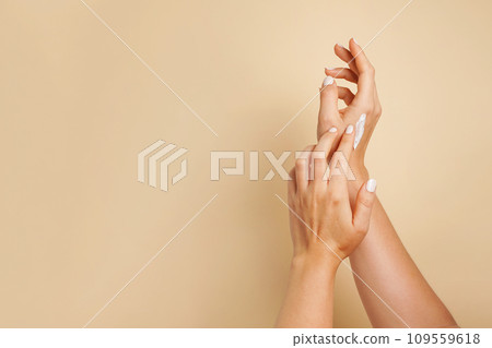 Beautiful young woman hands with cosmetic cream. Woman applies cream on her hands on beige background, copy space 109559618