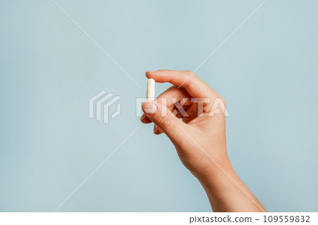 White pill in female hand on blue background, Taking Your Medication 109559832