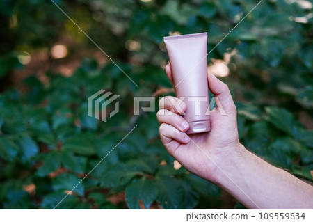 Man holding beige tube of facial cream on nature background. Mockup for design Man holding beige tube of facial cream on nature background. Mockup for design 109559834