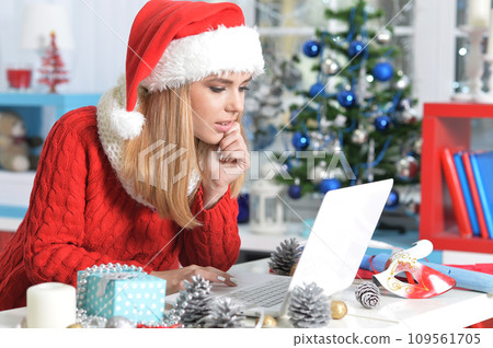 Happy young woman using laptop preparing for Christmas Happy young woman using laptop preparing for Christmas 109561705