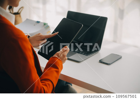 Attractive smiling young asian business woman work at home office, Asian woman working on laptop computer holding tablet. 109567501
