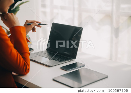 Attractive smiling young asian business woman work at home office, Asian woman working on laptop computer holding tablet. 109567506