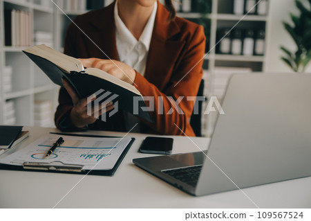 Attractive smiling young asian business woman work at home office, Asian woman working on laptop computer holding tablet. 109567524