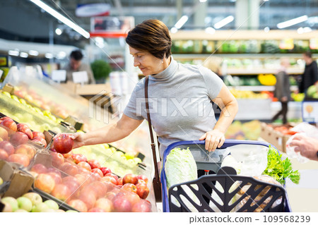 Positive woman chooses ripe red apples on grocery store window 109568239
