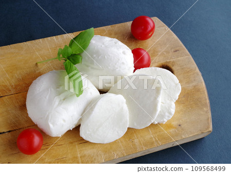 Mozzarella cheese, red tomatoes, green basil on a wooden plate, black background 109568499