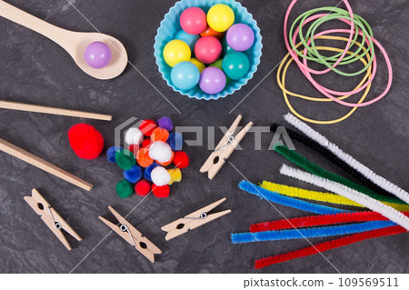 Colorful pompoms, balls and rubber erasers with spoon and tongs. Development of kids motor skills 109569511