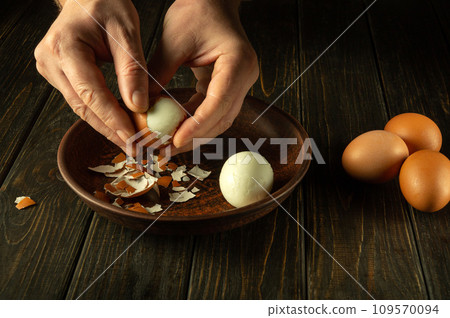 Preparing a delicious breakfast with boiled eggs on the kitchen table. Peeling an egg from the shell by a man hands. Egg diet concept 109570094
