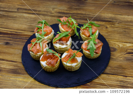 Tartlets with salmon, cream cheese and arugula on wooden table Tartlets with salmon, cream cheese and arugula on wooden table 109572196