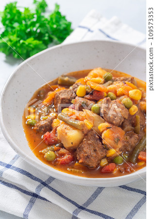 Beef stew with potato, green beans, carrot, peas and corn, in gray bowl, vertical 109573353
