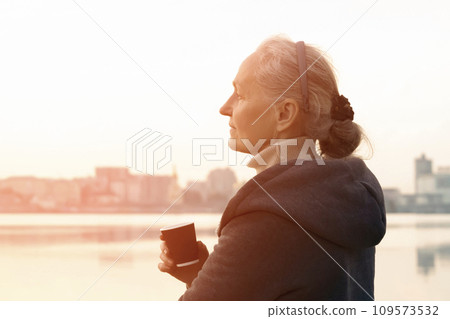 A woman, lady drinks a coffee and enjoys the sunset. 109573532