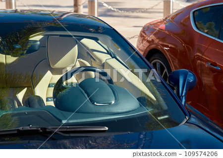 Two expensive sports cars stand side by side in sunny weather, a view of the bright interior through any glass 109574206