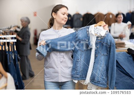 Middle-aged woman choosing jean jacket in clothing store Middle-aged woman choosing jean jacket in clothing store 109576583