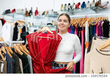 Smiling girl choosing colorful clothes in dressing room in showroom Smiling girl choosing colorful clothes in dressing room in showroom 109576584