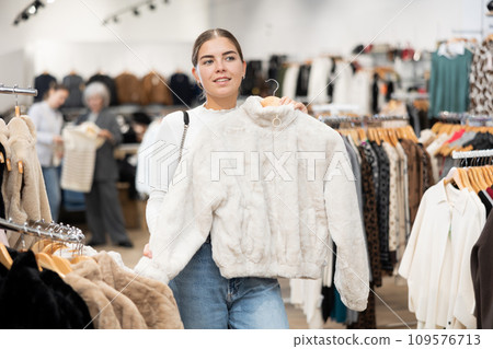 Young girl choosing short fur coat in clothing shop Young girl choosing short fur coat in clothing shop 109576713