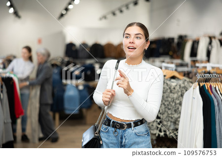 Positive joyful young woman looking for fashionable clothes in clothing boutique Positive joyful young woman looking for fashionable clothes in clothing boutique 109576753
