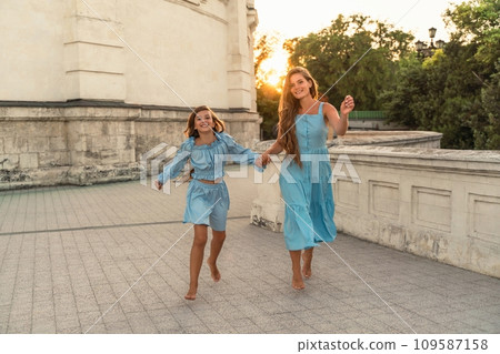Mother daughter sunset. in blue dresses with flowing long hair against the backdrop of sunset. The woman hugs and presses the girl to her. 109587158