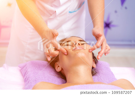 Relaxing massage. European woman getting facial massage in spa salon, side view Relaxing massage. European woman getting facial massage in spa salon, side view 109587207