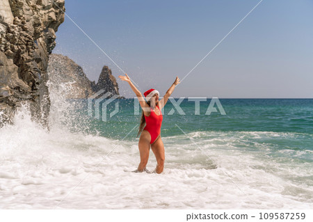 A woman in Santa hat on the seashore, dressed in a red swimsuit. New Year's celebration in a hot country. 109587259