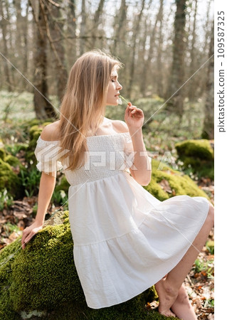 Snowdrops galanthus blonde. A girl in a white dress sits on a meadow with snowdrops in a spring forest 109587325