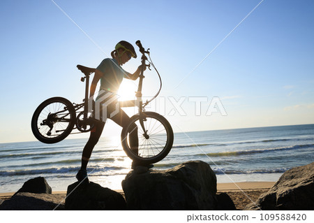 Woman carrying a folding bike on sunrise seaside road Woman carrying a folding bike on sunrise seaside road 109588420