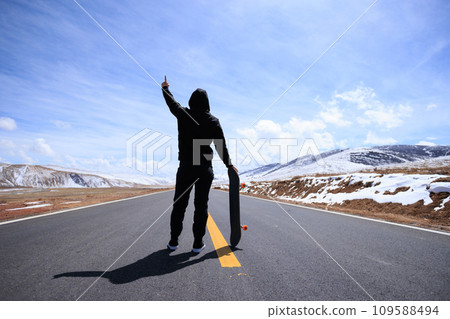 Skateboarder skateboarding on snowy country road Skateboarder skateboarding on snowy country road 109588494