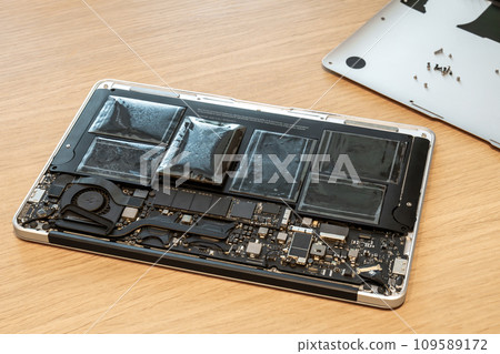 Swollen battery of broken laptop in open casing closeup Swollen battery of broken laptop in open casing closeup 109589172