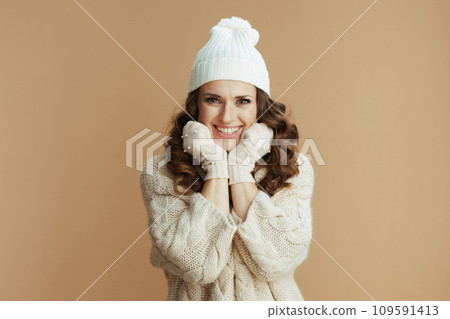 smiling woman in beige sweater, mittens and hat against beige smiling woman in beige sweater, mittens and hat against beige 109591413