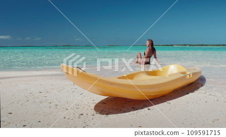 Woman relax sitting on beach, yellow kayak on sand, blue sky, turquoise water. Tanned young female on tropical island back view. Outdoor lifestyle travel on summer holiday vacation, active sport 109591715