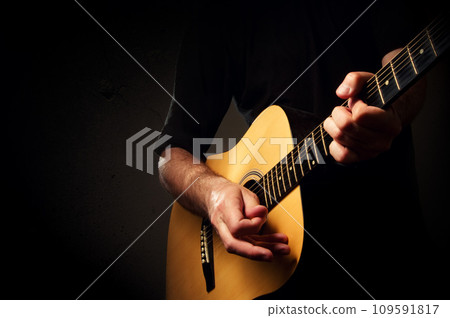 Man playing acoustic guitar in low light environment. Acoustic guitarist concert, unplugged performance. 109591817