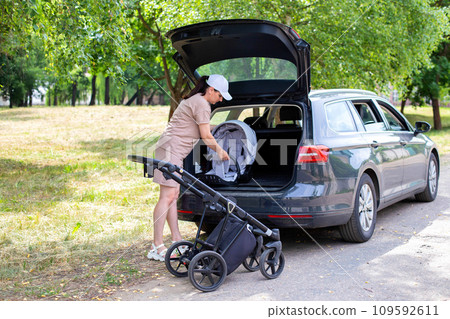 The caucasian girl puts the baby stroller in the trunk of the car. The concept of a spacious trunk in a family car. The caucasian girl puts the baby stroller in the trunk of the car. The concept of a spacious trunk in a family car. 109592611