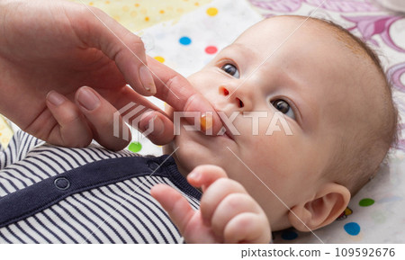 A mother massages the gums of a baby boy during the eruption of the first teeth, close-up A mother massages the gums of a baby boy during the eruption of the first teeth, close-up 109592676