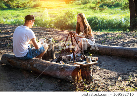 Young caucasian guy and girl sit on logs in nature and communicate. Outdoor recreation in summer, relaxation. Young caucasian guy and girl sit on logs in nature and communicate. Outdoor recreation in summer, relaxation. 109592710