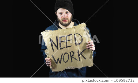 Homeless holds piece of cardboard with inscription Need Work. Refugee is looking for job. Male tramp in dirty clothes, black background. Poverty. Bearded fugitive beggar. Immigrant. Drunkenness 109592732
