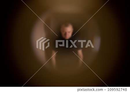 A male apartment burglar stands on the stairwell and peers through the peephole, close-up. The concept of theft in apartments, blurry 109592748