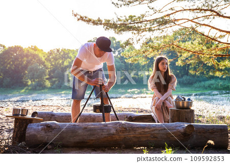 A young caucasian girl and a guy are resting in nature in the summer. Beautiful landscape on the banks of the river and forest. Picnic and tourism. A young caucasian girl and a guy are resting in nature in the summer. Beautiful landscape on the banks of the river and forest. Picnic and tourism. 109592853