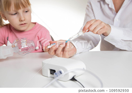 A doctor is putting a drug into a nebulizer for the treatment of respiratory diseases in a little girl 5 years old. Inhalation for the treatment of bronchitis and pneumonia A doctor is putting a drug into a nebulizer for the treatment of respiratory diseases in a little girl 5 years old. Inhalation for the treatment of bronchitis and pneumonia 109592930