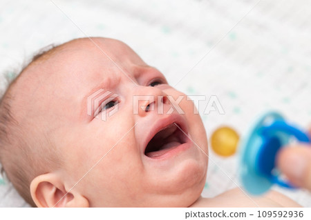 Little baby boy crying with a pacifier in his mouth. The concept of weaning the habit of sucking a pacifier in children, close-up. Copy space for text 109592936