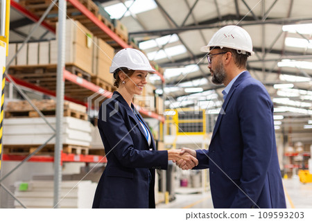 Female engineer and male project manager shaking hands in modern industrial factory. Manufacturing facility with robotics and automation. Women in manufacturing. 109593203