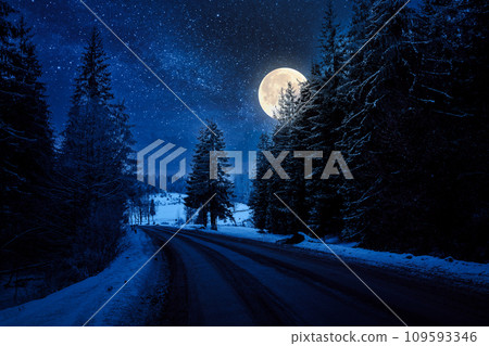 asphalt country road through forested countryside in winter at night. trees and hills in snow. mysterious atmosphere in full moon light asphalt country road through forested countryside in winter at night. trees and hills in snow. mysterious atmosphere in full moon light 109593346