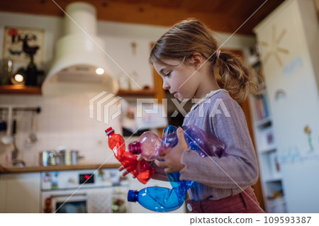 Girl throwing plastic bottles into recycling bin. Daughter sorting the waste according to material into colored bins. 109593387