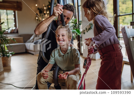Father and vacuuming son's hair with vacuum cleaner. Father with kids cleaning house, helping with house chores. 109593390