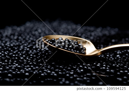 Closeup of natural black caviar on a golden spoon on black background, texture of fresh sturgeon caviar macro photo. Closeup of natural black caviar on a golden spoon on black background, texture of fresh sturgeon caviar macro photo. 109594125