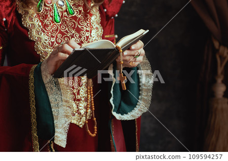 Closeup on medieval queen in red dress with book and rosary 109594257