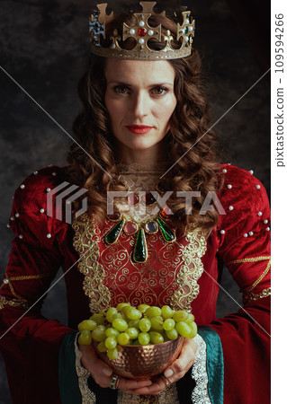 medieval queen in red dress with plate of grapes and crown 109594266