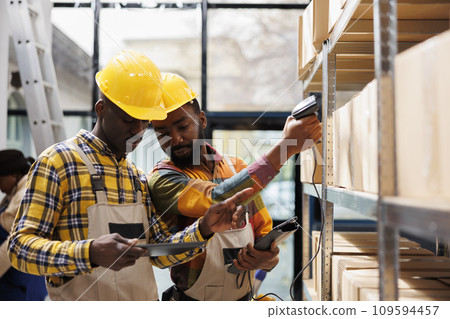 African american warehouse managers scanning parcels before shipment. Post office storehouse workers doing merchandise inventory using scanner and checking barcode in digital tablet African american warehouse managers scanning parcels before shipment. Post office storehouse workers doing merchandise inventory using scanner and checking barcode in digital tablet 109594457