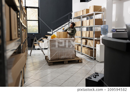 African american manager preparing clients orders, putting adhesive tape on cardboard box before delivering packages. Stockroom employee working at merchandise inventory in storage rooom 109594582