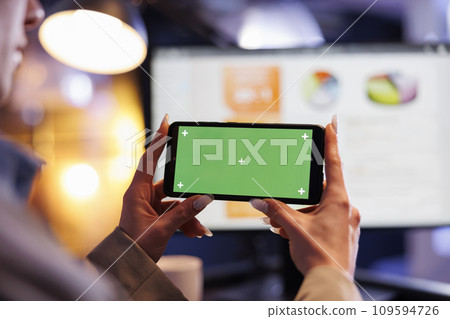 Businesswoman holding smartphone with green screen chroma key mock up display, working late at night in startup office. Executive manager analyzing marketing graphs report. Business concept Businesswoman holding smartphone with green screen chroma key mock up display, working late at night in startup office. Executive manager analyzing marketing graphs report. Business concept 109594726