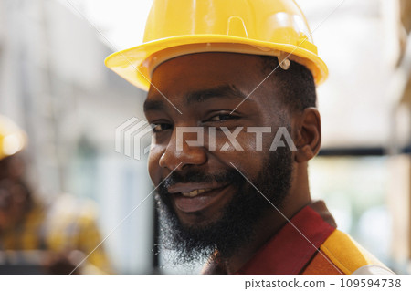 Smiling african american handyman wearing yellow hard hat portrait. Delivery service company loader in protective industrial equipment looking at camera in warehouse close up 109594738