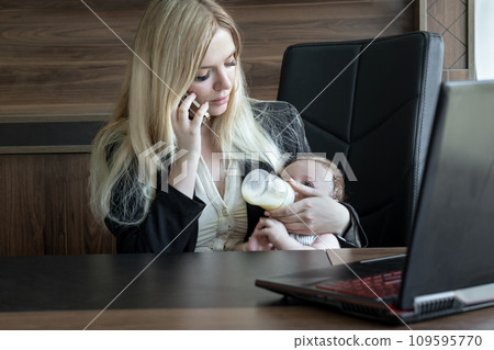 Young business woman feeds baby from bottle in office and talks on phone, concept of combining business and caring for newborn baby. 109595770