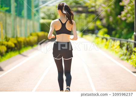 Rear view of a young woman in sportswear running in the greenery Rear view of a young woman in sportswear running in the greenery 109596237